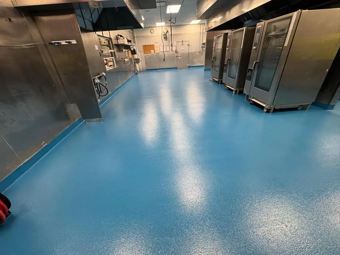 A commercial kitchen with blue epoxy flooring by a top Bohemia, NY contractor; ovens line the right side.
