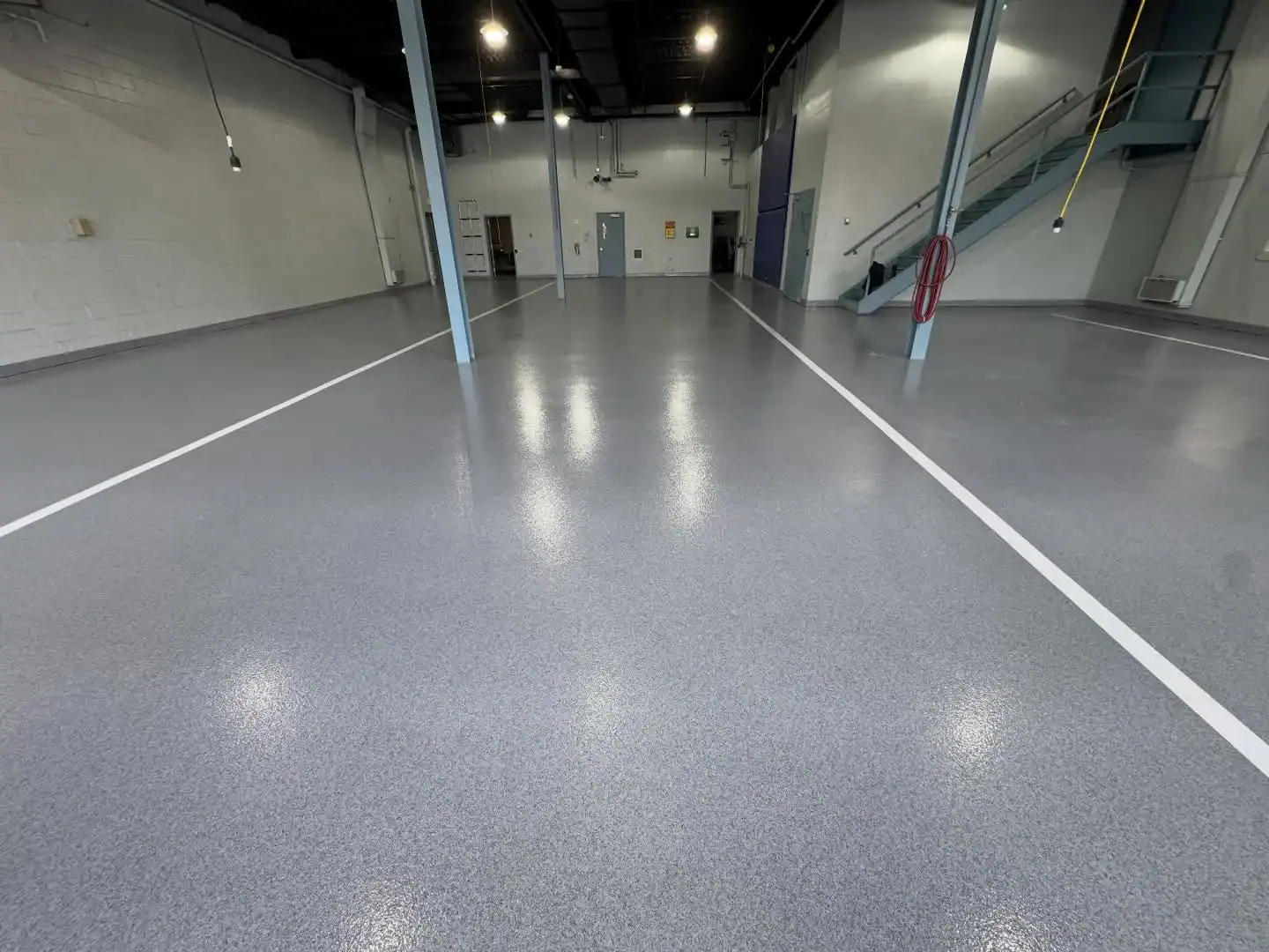 Spacious NY industrial space features shiny epoxy flooring, blue beams, and a staircase by Bohemia contractor.