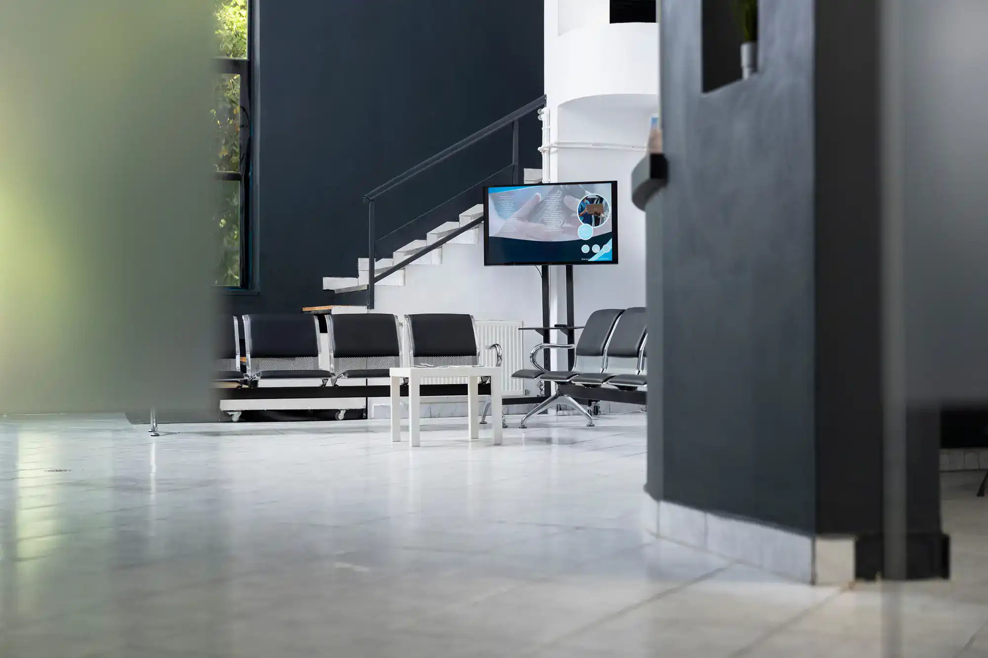 Modern waiting room in Bohemia, NY with epoxy floors, empty chairs, a table, and a wall-mounted TV.