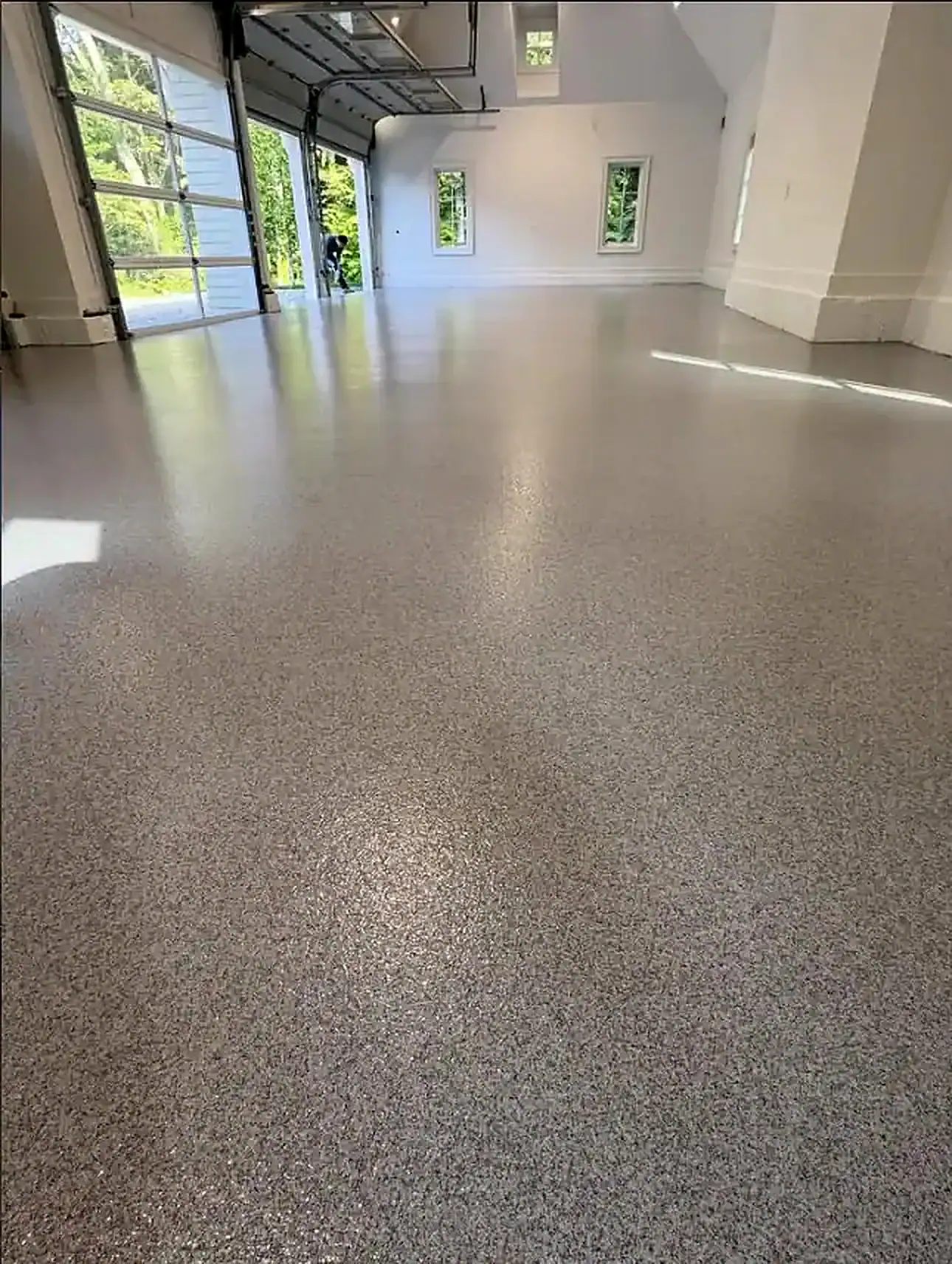 Spacious NY garage features a shiny speckled epoxy floor by Epoxy Flooring Contractor Bohemia with sunlight.