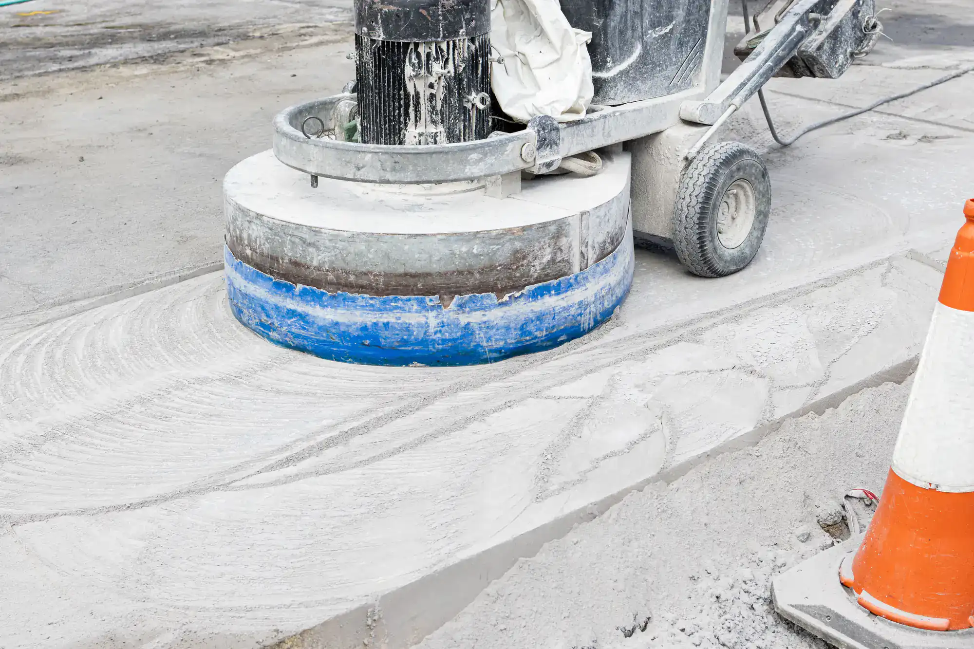A concrete grinder smooths a sidewalk next to an Epoxy Flooring Contractor Bohemia,NY cone on the right.