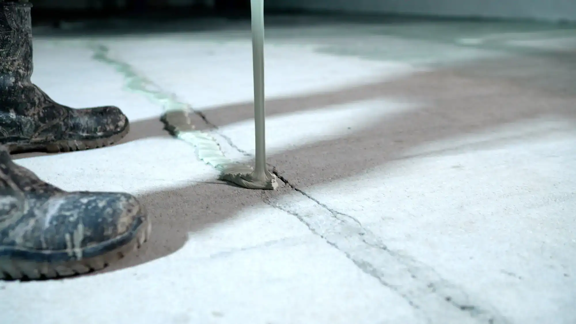 Epoxy Flooring Contractor Bohemia repairs a floor crack with material while muddy shoes sit close by.