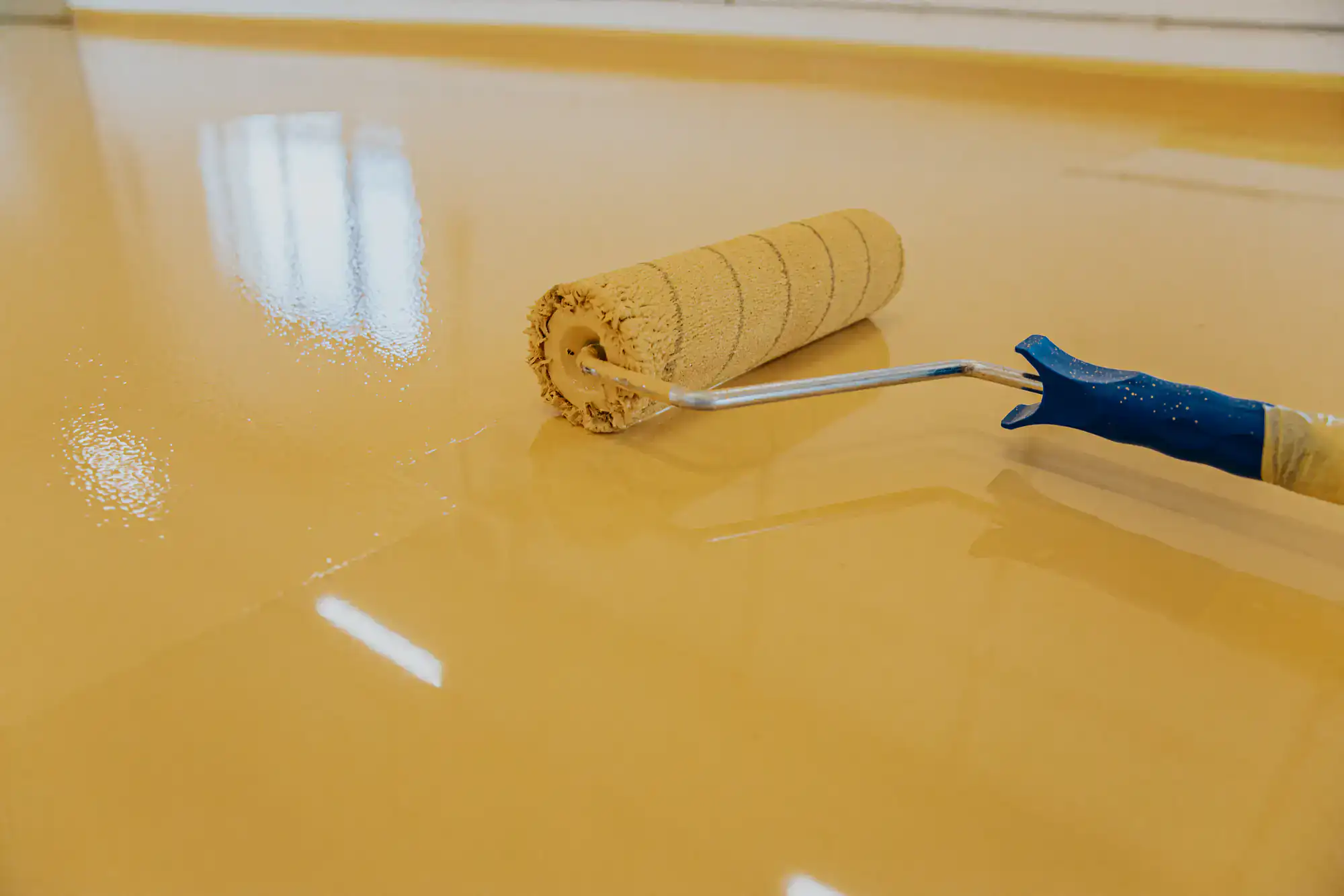 A paint roller spreads glossy yellow epoxy floor coating, expertly applied by a contractor in Bohemia, NY.