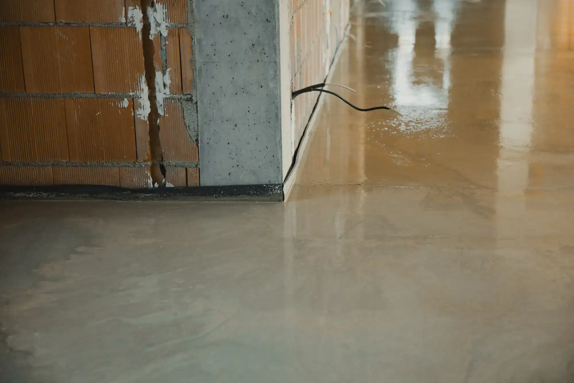 A partially finished wall with exposed bricks and a shiny epoxy concrete floor by a NY Epoxy Flooring Contractor.