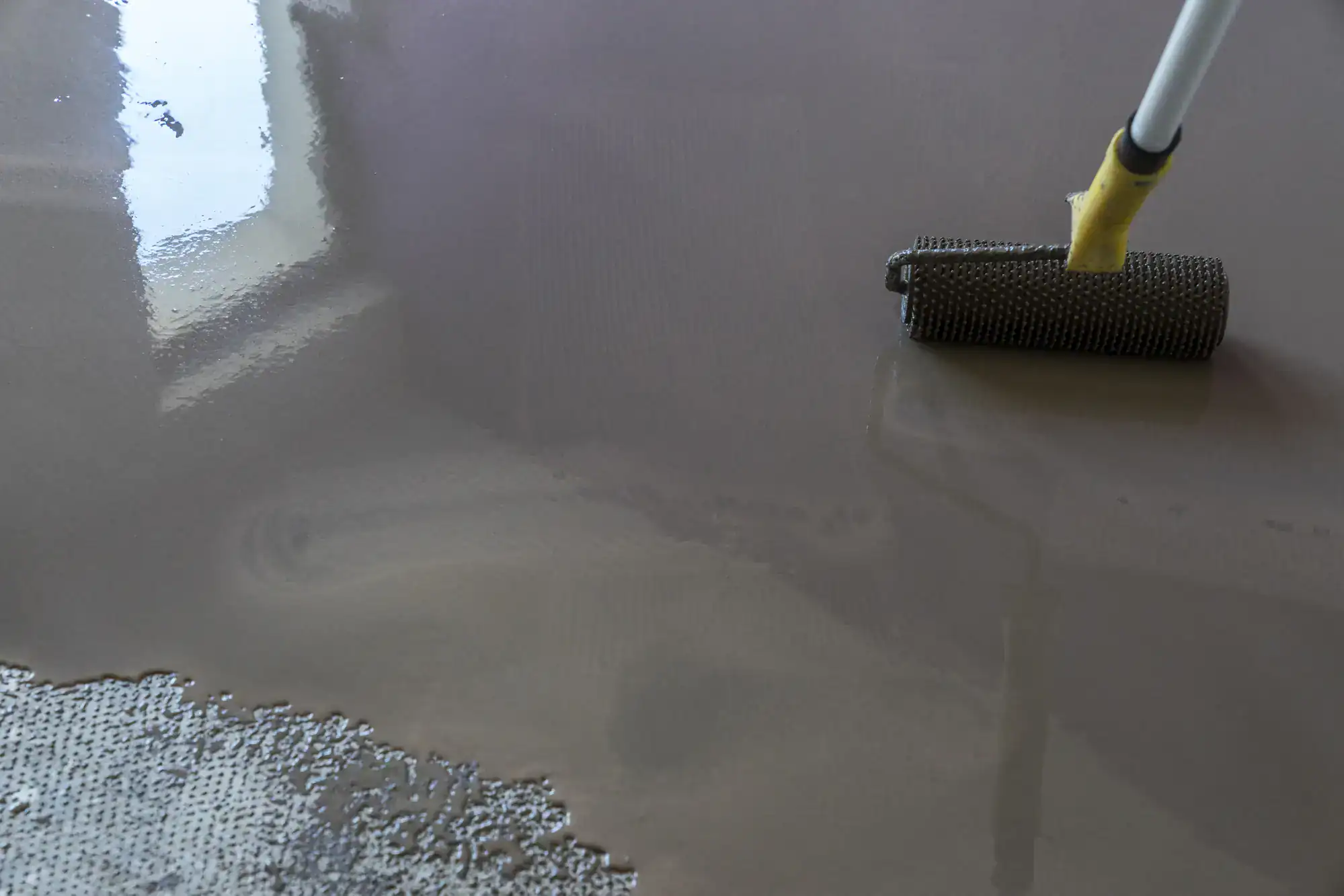 A spiked roller levels wet concrete, a common step for NY or Epoxy Flooring Contractor Bohemia projects.