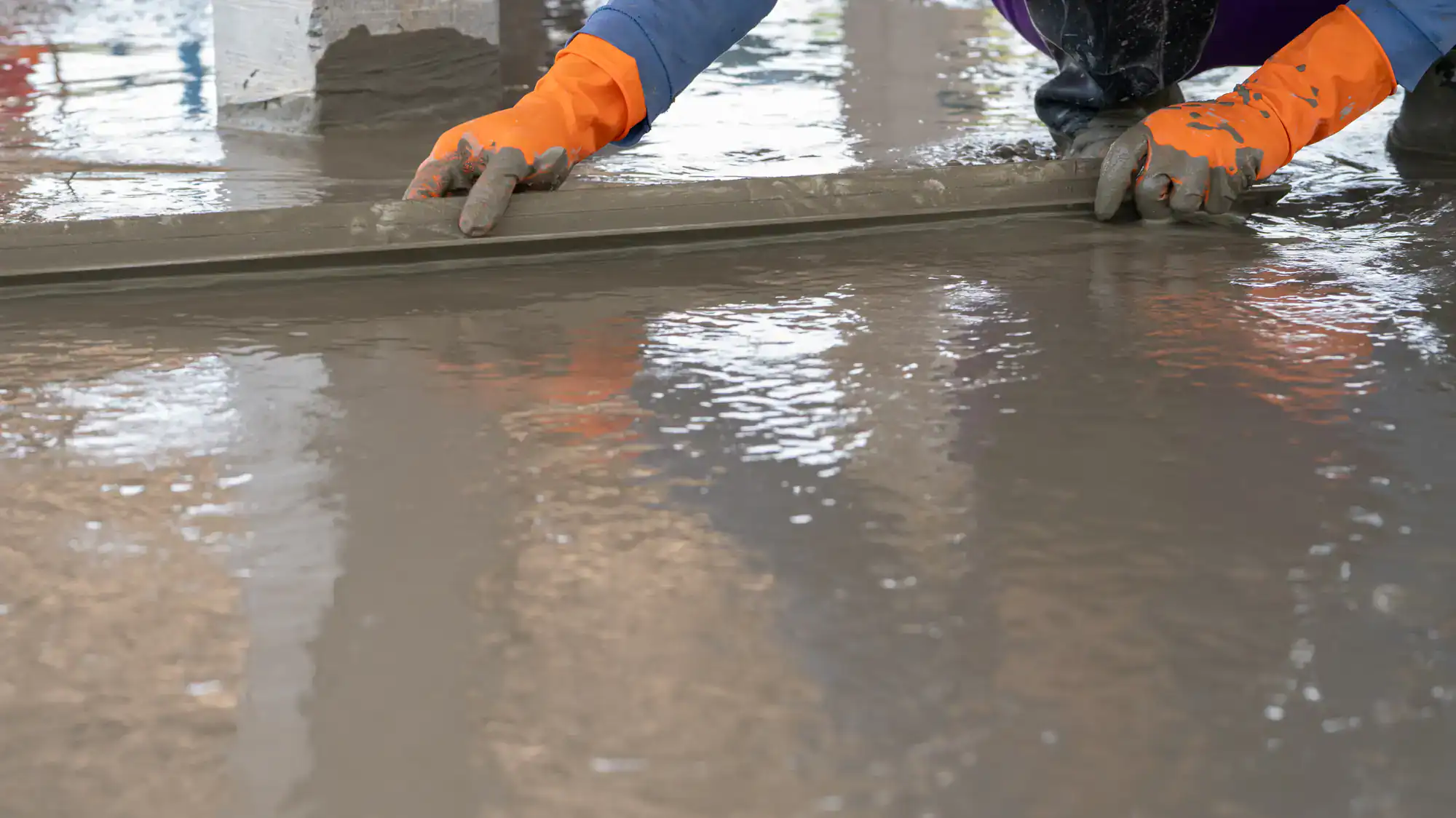 A worker in orange gloves smooths wet concrete on a shiny floor prepped by NY Epoxy Flooring Contractor.