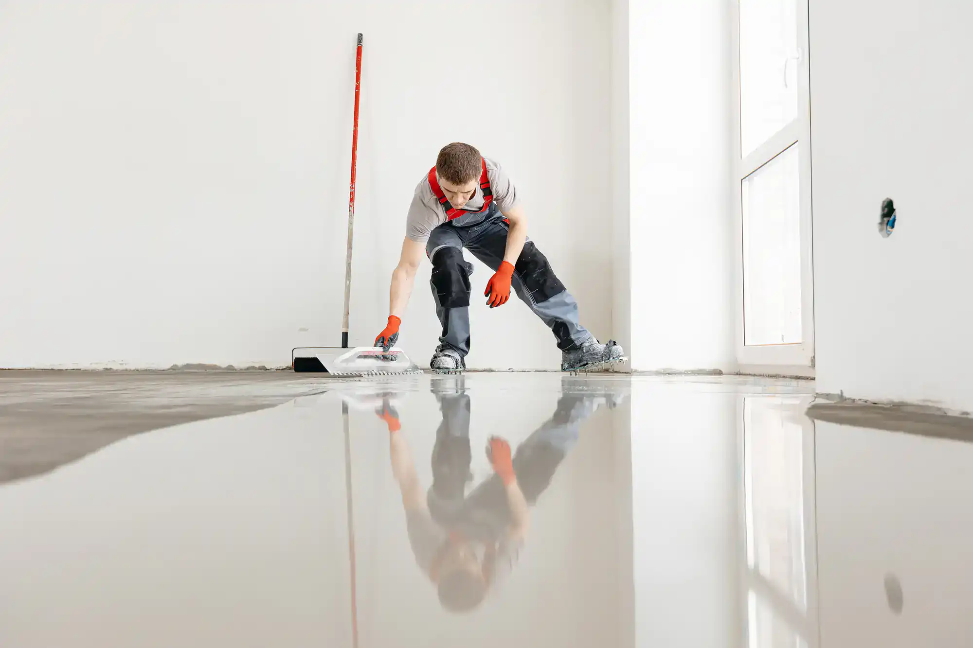 An Epoxy Flooring Contractor in Bohemia, NY applies liquid cement to a bright floor near a mop and window.